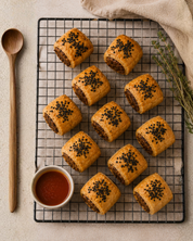 Baked pastries with a dipping sauce on a cooling rack, with a wooden spoon and towel in the background.
